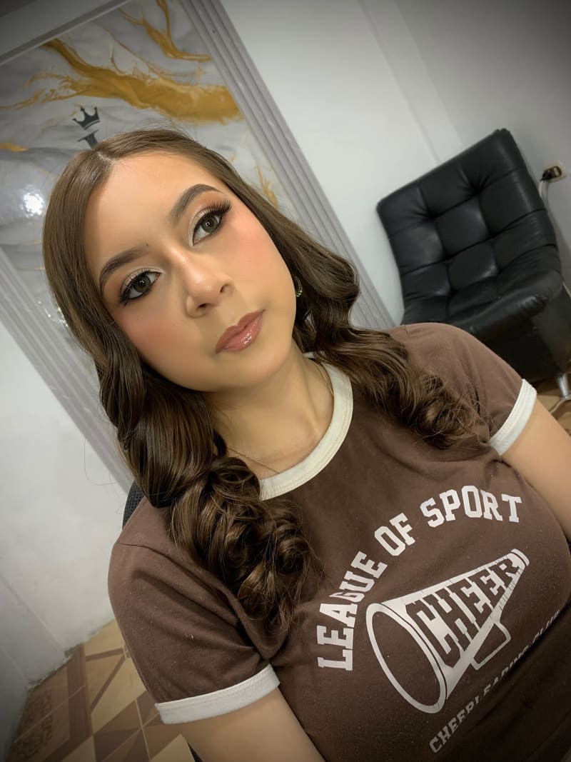 Quinceañera con maquillaje luminoso, pestañas definidas y cabello en ondas