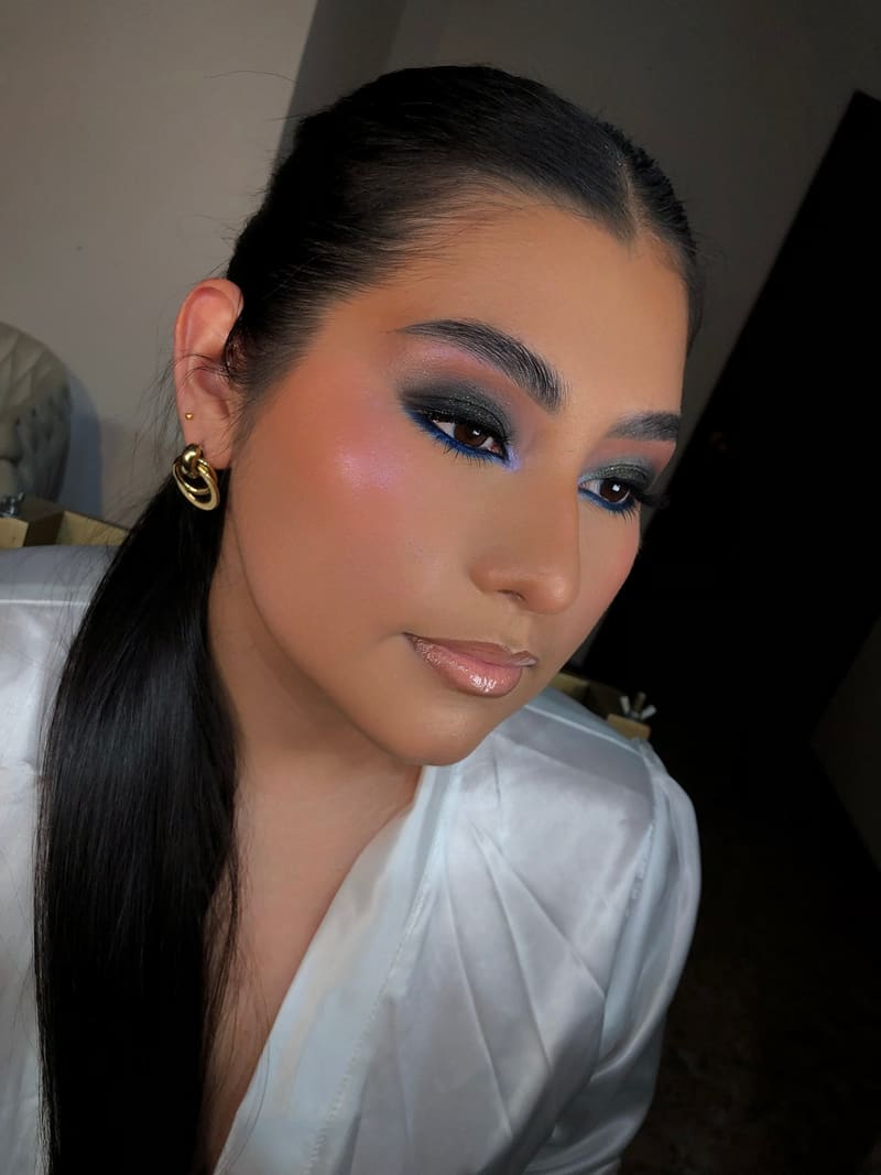 Maquillaje de noche con sombra verde esmeralda, delineado azul eléctrico y labios con brillo